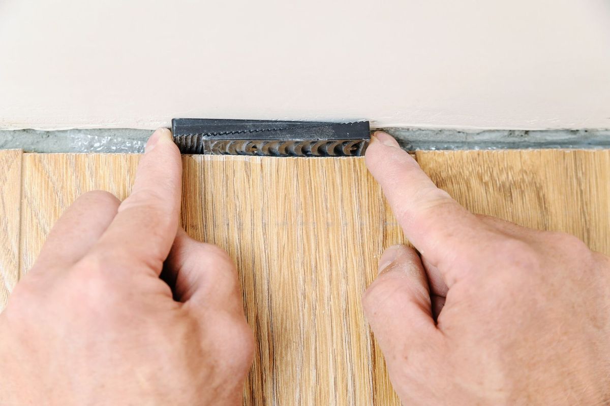 Worker's hands placing wedges between the wall and the floorboard