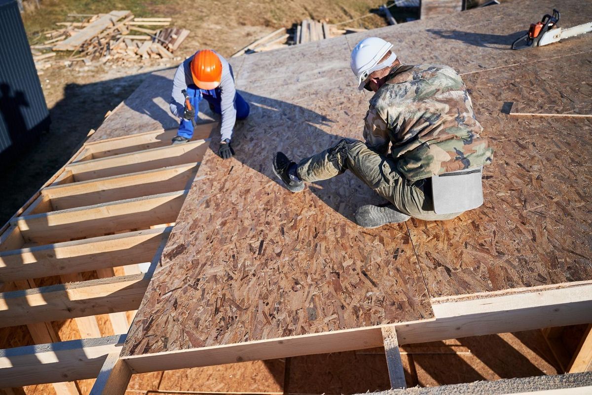 Carpenter hammering nail into osb panel while building wooden frame house