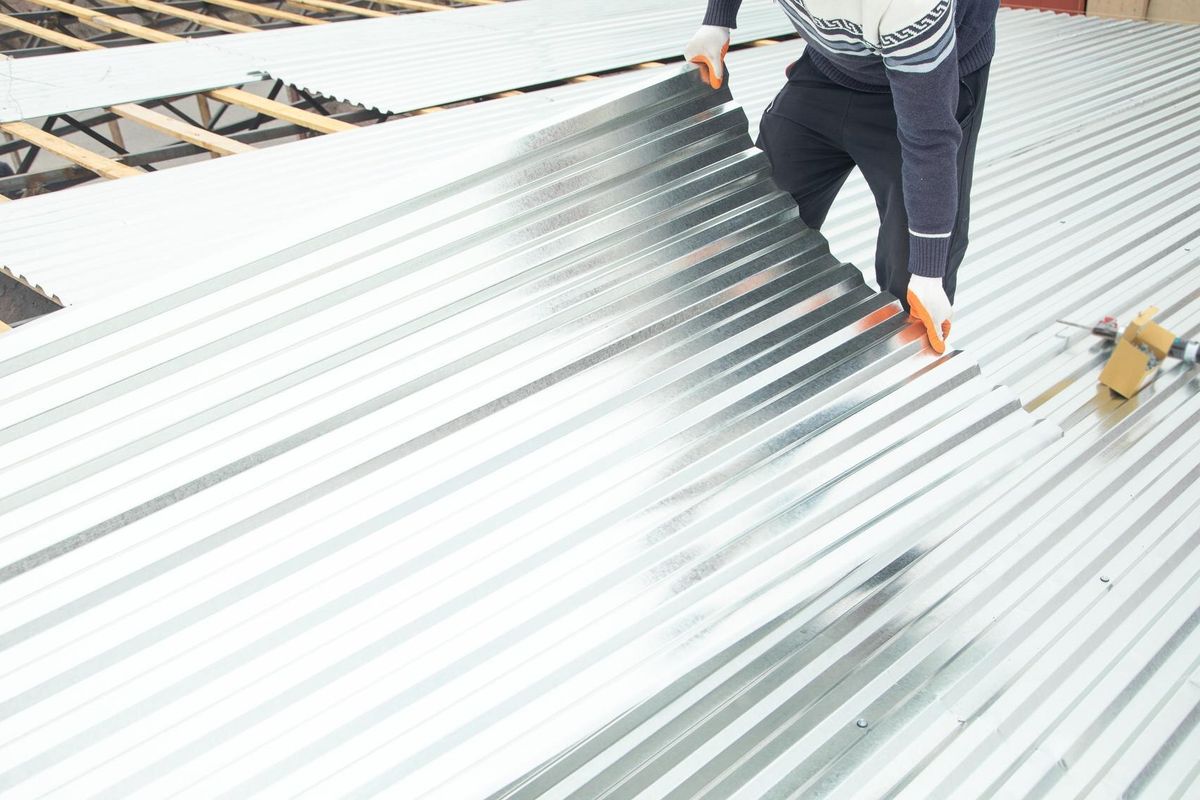 Worker puts the metal tiles on the roof of a house