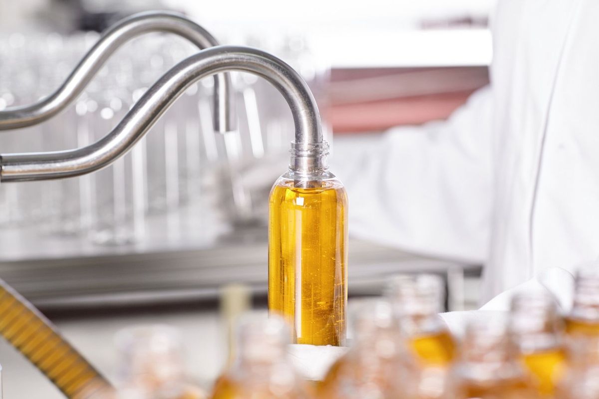 Factory worker in white gown and rubber gloves holding plastic bottle