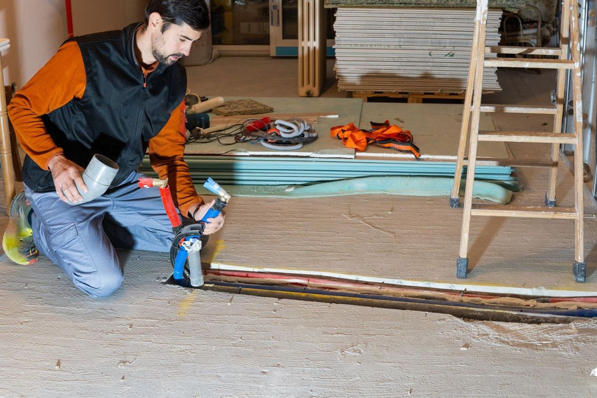 plumber installing pipes in the floor of a house under renovation with a lot of work materials