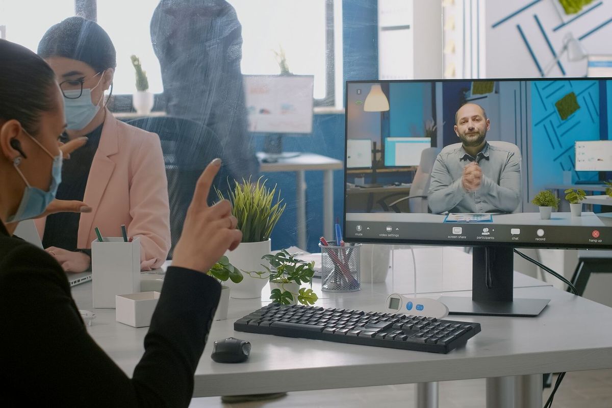 Freelancer wearing protective face mask during online videocall sitting at desk in startup company office. Coworkers working on computer during coronavirus global pandemic