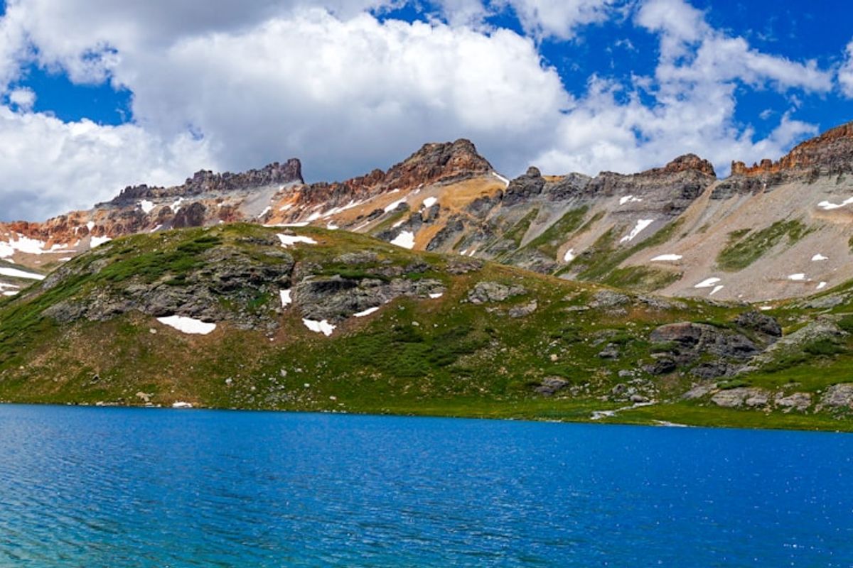 green and white mountains near blue sea under blue and white cloudy sky during daytime