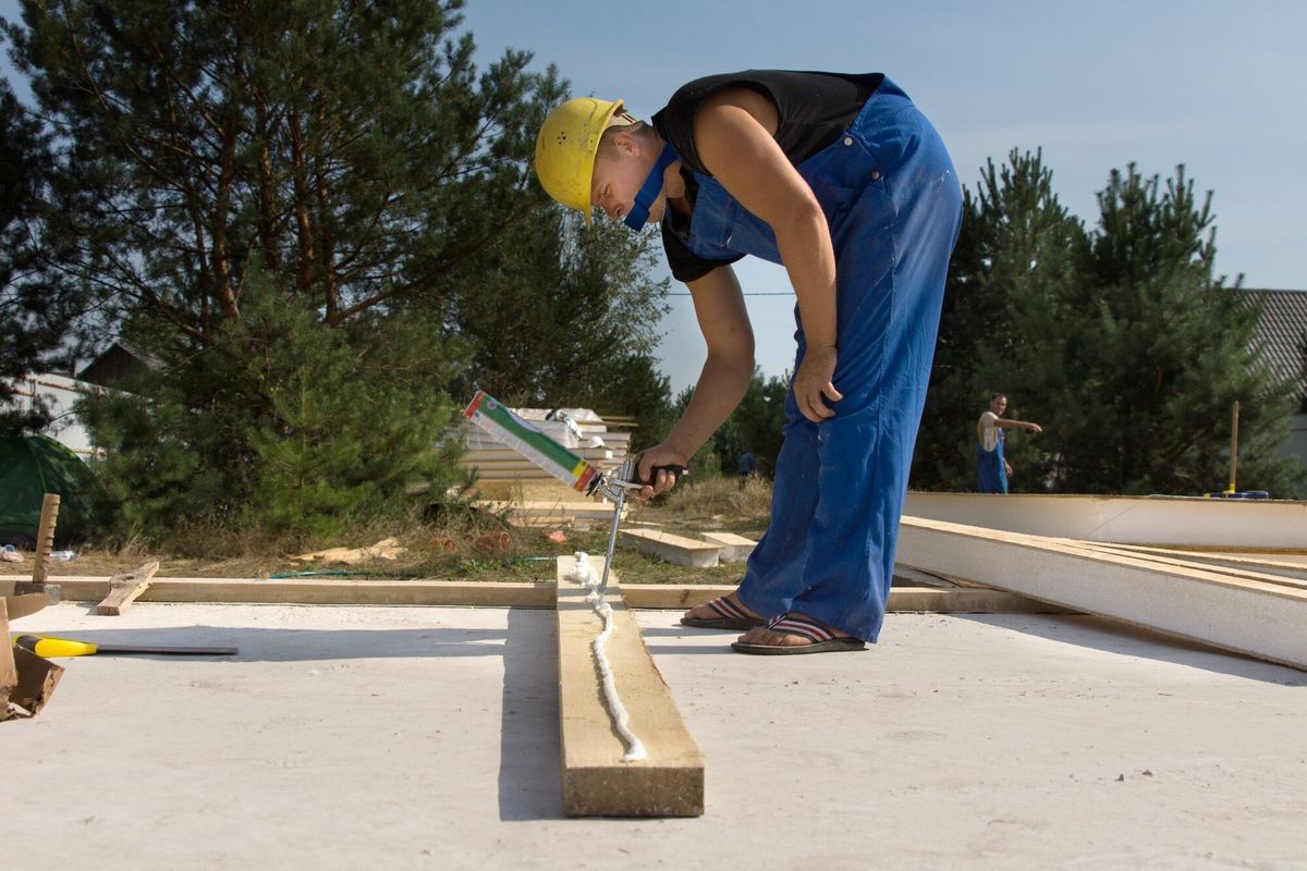 Builder or carpenter applying glue to a wooden beam on a construction site from a glue gun