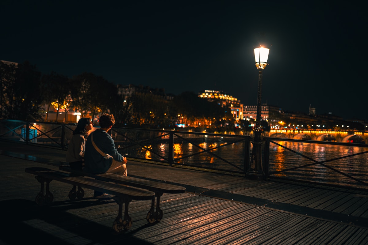 two people sitting on a bench next to a body of water