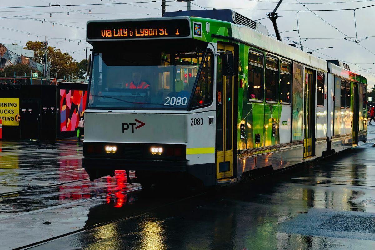 A melbourne tram travels on a wet road.