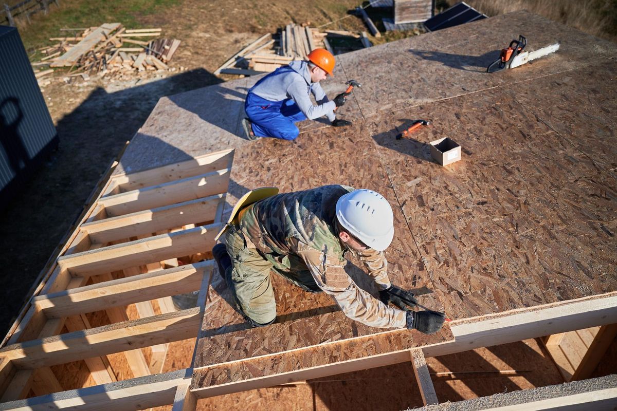 Carpenter hammering nail into osb panel while building wooden frame house