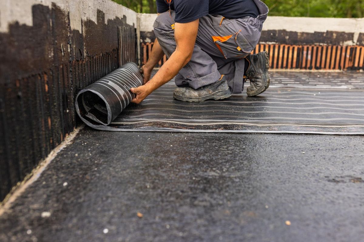 Worker laying the vapor barrier for the roof bituminous membrane to be welded with flame