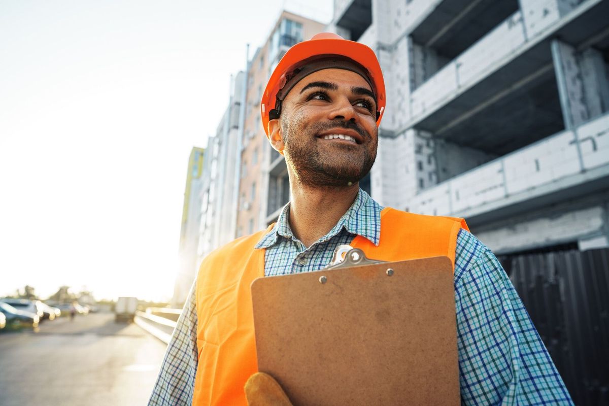 Young man engineer in workwear standing in construction site with clipboard