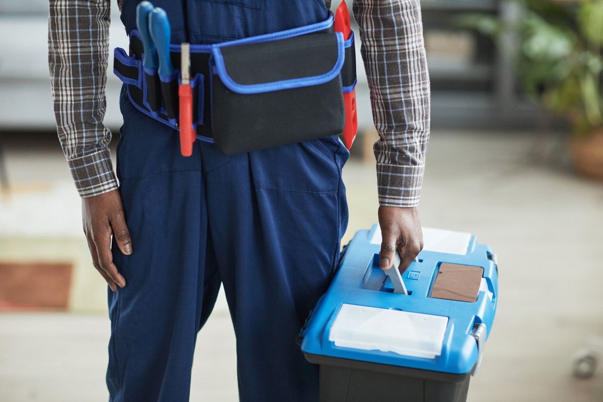 Cropped shot of unrecognizable African-American handyman holding toolbox while standing in home interior, copy space