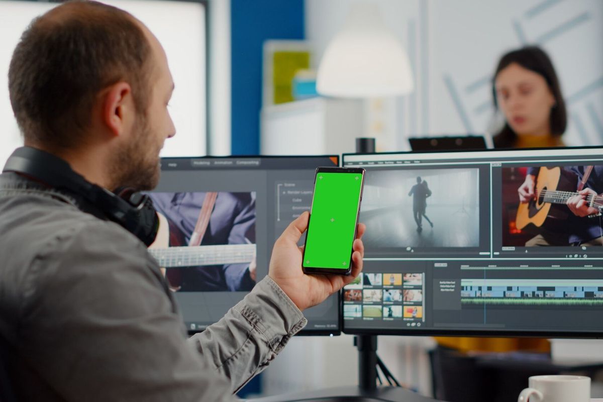 Video editor talking on video call holding smartphone with green screen