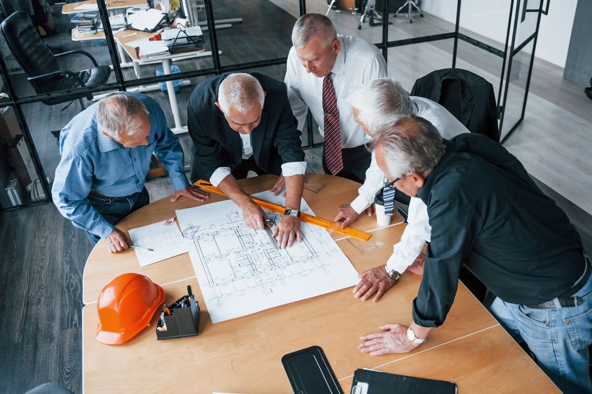 Aged team of elderly businessman architects works with plan in the office.